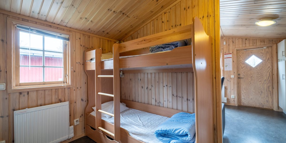 Interiör av campingstuga med våningssäng, träväggar och fönster mot veranda