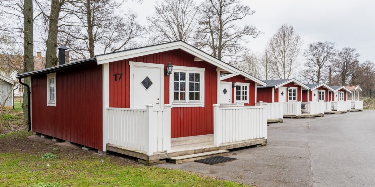 Rad av röda campingstugor med vita knutar och verandor längs asfalterad väg